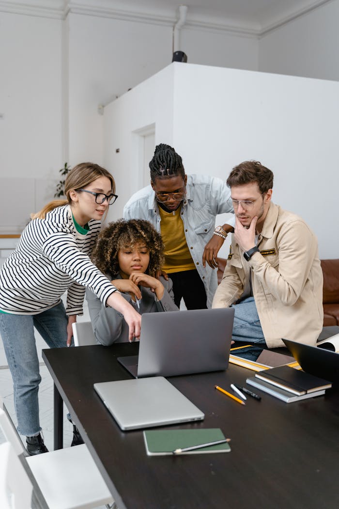 Diverse group of coworkers collaborating on a project using a laptop in a modern office.